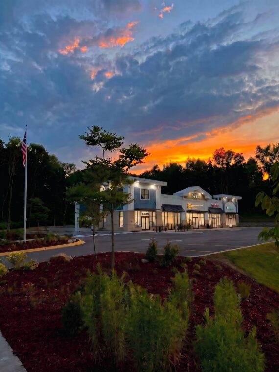 Hamptons Plaza of Oshtemo retail plaza lit at sunset with flag and landscaping, 6289 West Main Street, Oshtemo Township, Kalamazoo, Michigan